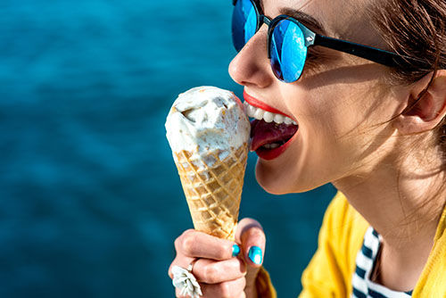 Young woman in yellow sweater and sunglasses eating ice cream on the blue water background